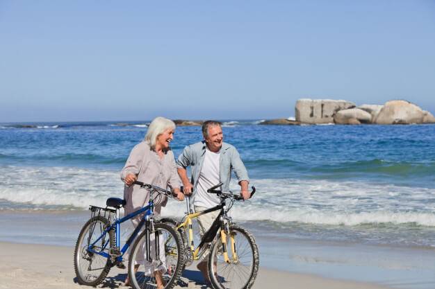 Two elderly people biking on the beach.